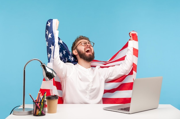 Delighted enthusiastic businessman raising American flag and screaming for joy in office workplace celebrating labor day or US Independence day 4th of july government support studio shot isolated