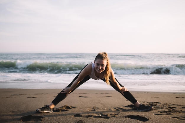 Photo delighted female practicing yoga position on coastline