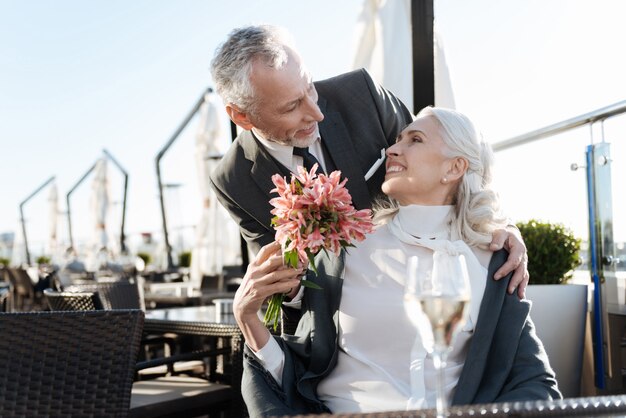 Delighted female turning her head while smiling to her boyfriend and taking nice flowers