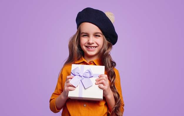 Delighted girl in hat showing gift box