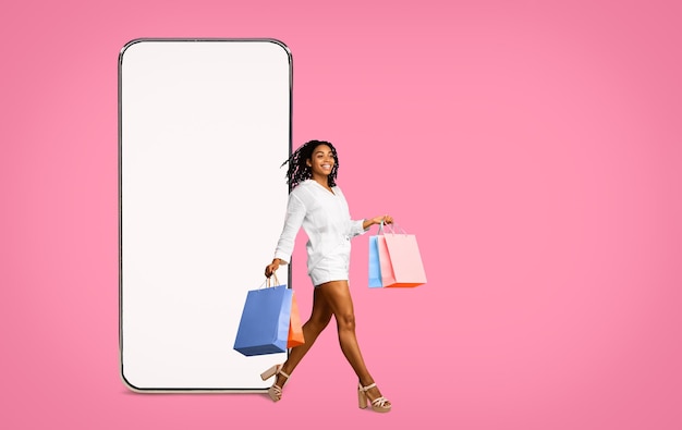 Delighted hot black young woman with purchases and cell phone