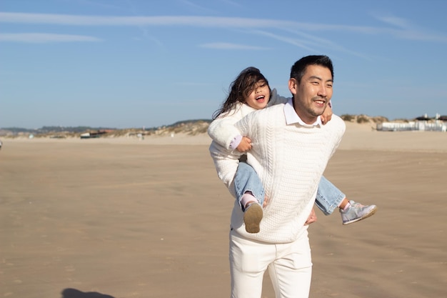 晴れた日に一緒に喜んでいる日本の家族。父と娘が遊んで、背中に乗って、浮気している。余暇、家族の時間、子育ての概念