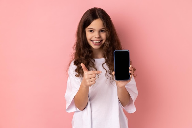 Delighted little girl showing smart phone with black blank screen pointing finger at display