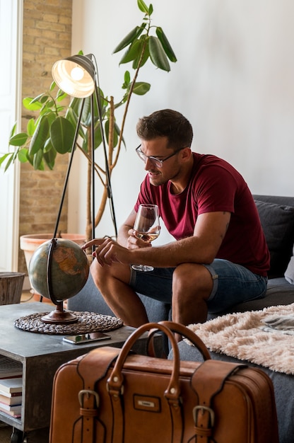 Delighted male traveler choosing country on planet Earth globe before adventure while sitting in room with suitcase
