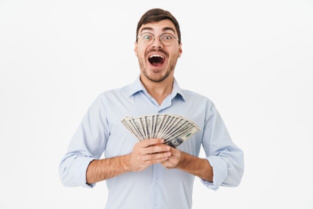 delighted man in eyeglasses holding dollars and expressing surprise isolated over white wall