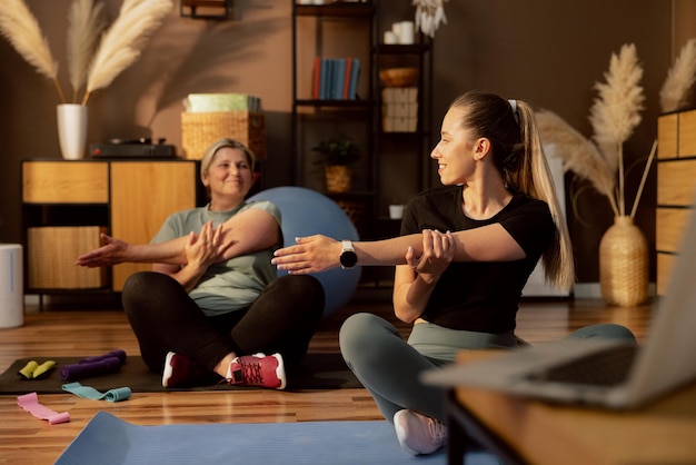 Delighted mother in background looking at adorable daughter doing stretching together