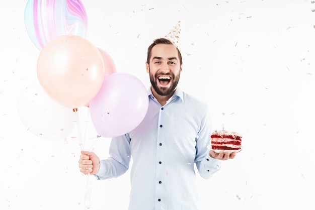 delighted party man laughing and holding birthday cake with air balloons isolated over white wall