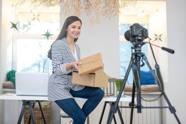 Delighted positive woman holding gift boxes while having a giveaway for her viewers