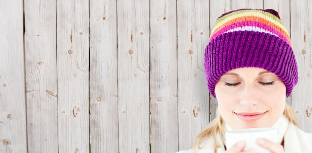 Foto donna contentissima con un cappello colorato e una tazza tra le mani su sfondo di legno