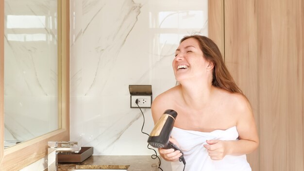 Delighted young woman dances and sings into hairdryer