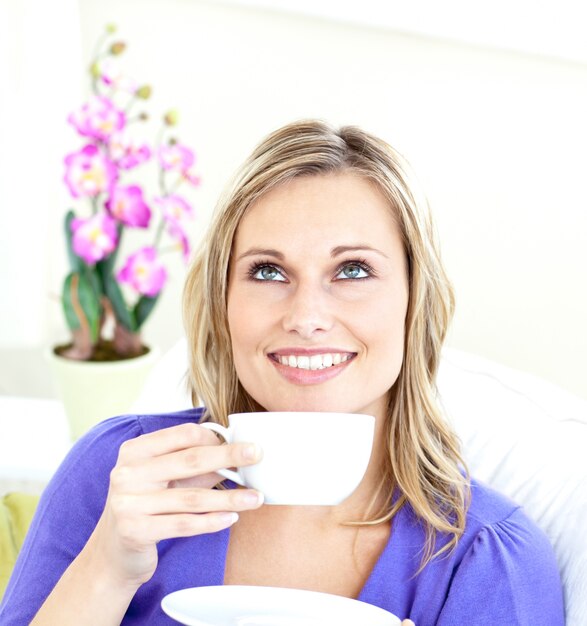 Delighted young woman holding a cup of coffee on a sofa