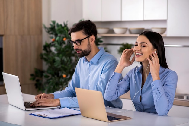 Delighteful work Cheerful young business woman listening to music while sitting at the table with his male colleague