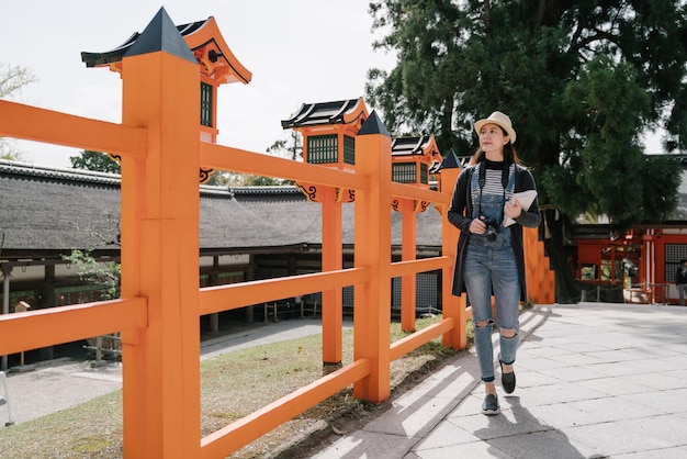 Delightful asian lady carrying a guide book is walking slowly along the orange fence. taiwanese woman is gazing afar and enjoy the magnificent distant view