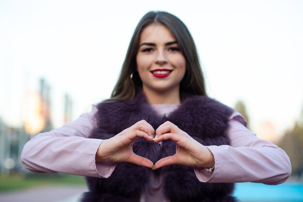 Delightful brunette model showing heart symbol with two hands over a city background