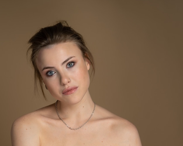 Delightful girl with heterochromia, nose piercing and plug in one ear, and strange hairstyle. With amazing professional makeup and silver chain around her neck. Beige background. Studio shot