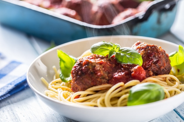 Вкусные итальянские мясные говяжьи шарики с макаронами, спагетти и базиликом в белой тарелке.
