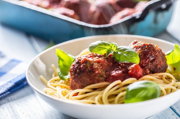 Polpette di carne di manzo del pasto italiano delizioso con spaghetti di pasta e basilico in piatto bianco.