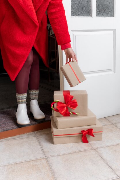 Deliver dressed in red coat holding Gift's Boxes near the white door on the eve of holidays Christmas