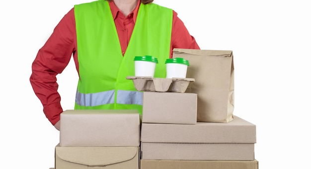 Deliver is in a green vest holding paper boxes and container take away with two white cups of coffee.