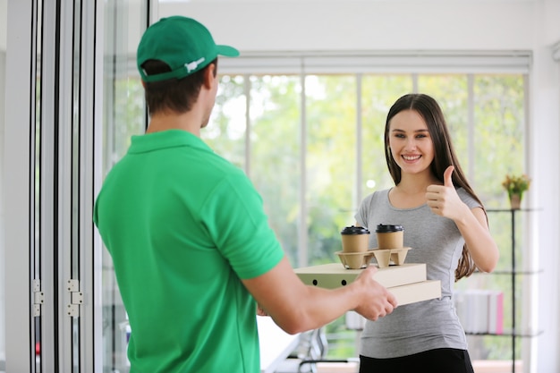 deliver man in green uniform handling bag of food, coffee cup give to female costumer in front of the house.