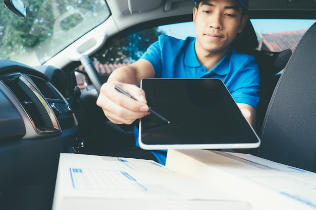 Deliver man holding tablet with parcels on seat in car. 