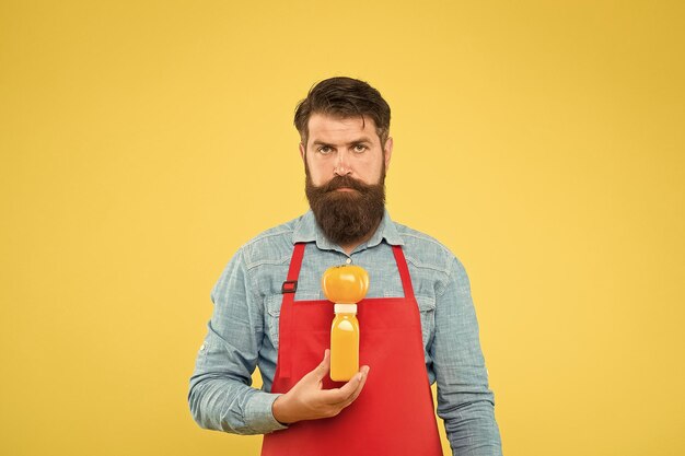 Delivering fresh vitamins Hipster smoothie beverage Man bearded chef hold organic natural tomato and bottle yellow background Vegetarian nutrition Smoothie drink Fresh juice Squeezing smoothie