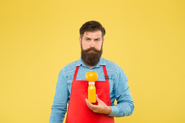 Delivering fresh vitamins. Hipster smoothie beverage. Man bearded chef hold organic natural tomato and bottle yellow background. Vegetarian nutrition. Smoothie drink. Fresh juice. Squeezing smoothie.