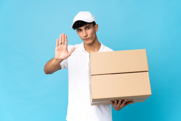 Delivery Argentinian man isolated on blue wall making stop gesture