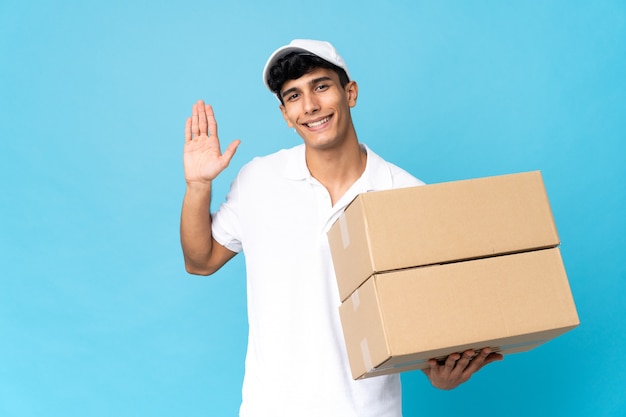 Delivery Argentinian man isolated on blue wall saluting with hand with happy expression