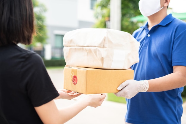 Consegna l'uomo asiatico indossa una maschera protettiva in uniforme blu e pronto per l'invio della consegna del sacchetto di cibo