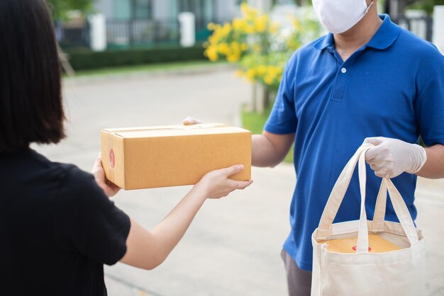 사진 배달 아시아 남자는 파란색 유니폼을 입고 보호 마스크를 쓰고 음식 가방을 배달할 준비가 되어 있습니다.