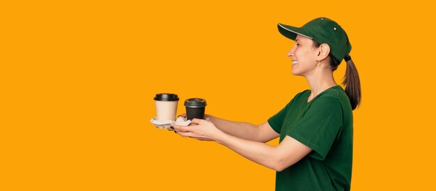 Delivery or barista woman wearing green and handing two cups of coffee