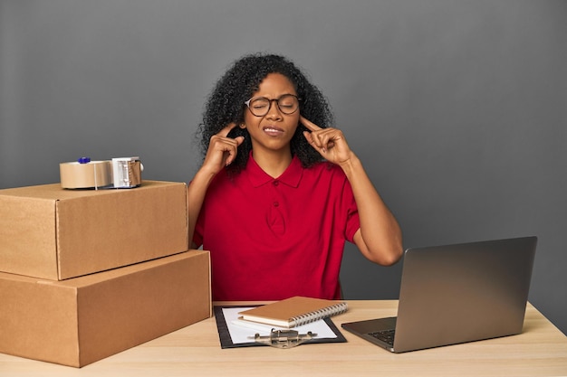 Delivery businesswoman with inventory and boxes covering ears with fingers stressed