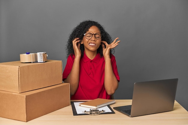 Delivery businesswoman with inventory and boxes covering ears with hands