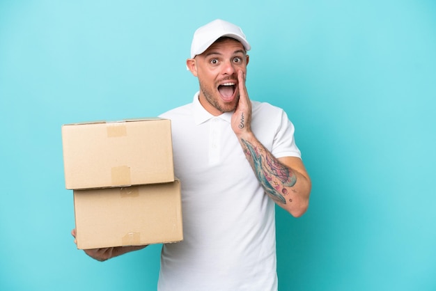 Delivery caucasian man isolated on blue background with surprise and shocked facial expression