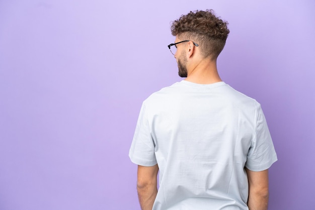 Delivery caucasian man isolated on purple background in back position and looking side