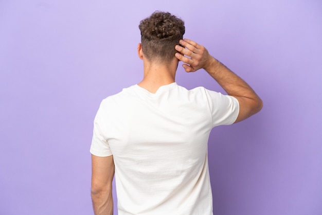 Delivery caucasian man isolated on purple background in back position and thinking