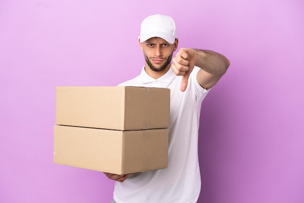 Delivery caucasian man isolated on purple background showing thumb down with negative expression