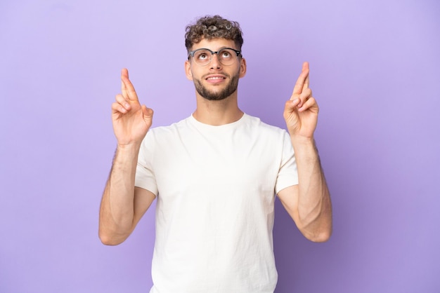 Delivery caucasian man isolated on purple background with fingers crossing and wishing the best