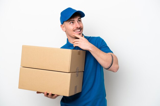 Delivery caucasian man isolated on white background looking up while smiling