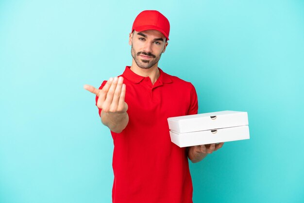 Consegna uomo caucasico che raccoglie scatole di pizza isolate su sfondo blu invitando a venire con la mano felice che tu sia venuto
