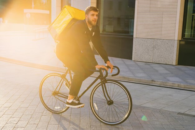 Delivery in the city A delivery man rides a bicycle around the city with a yellow bag The setting sun Delivery to the pandemic