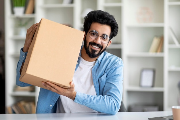 Delivery concept happy indian man showing big cardboard box at camera