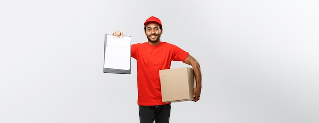 Delivery concept portrait of handsome african american delivery\
man or courier showing a confirmation document form to sign\
isolated on grey studio background copy space