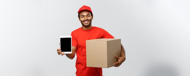 Delivery Concept Portrait of Handsome African American delivery man or courier with box showing tablet on you to check the order Isolated on Grey studio Background Copy Space