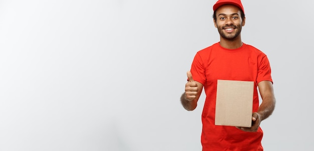 Delivery Concept Portrait of Happy African American delivery man holding a box package and showing thumps up Isolated on Grey studio Background Copy Space