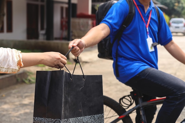 Delivery courier giving package order to customer while sitting on bicycle wearing backpack