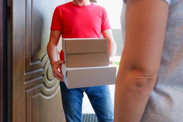 A delivery courier hands over cardboard boxes of goods to a woman near the door of her house