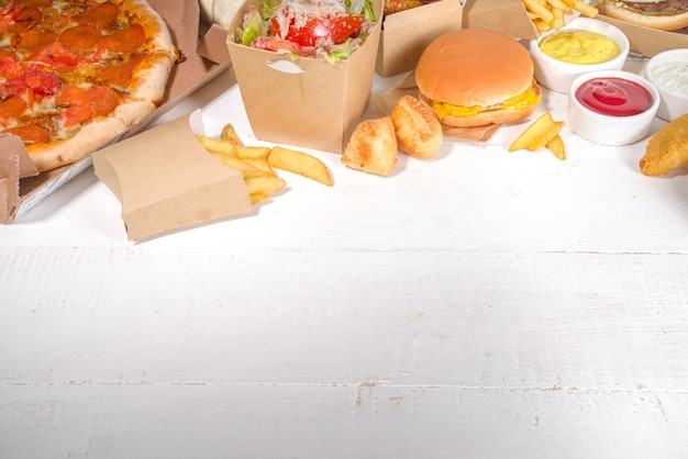 Delivery fastfood ordering food online concept. large set of\
assorted take out foods pizza, french fries, fried chicken nuggets,\
burgers, salads, chicken wings, various sides, white table\
background