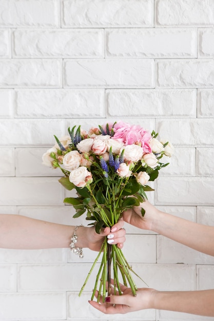 Delivery of a floral workshop. The customer receives his order-a bouquet of pink roses and wild flower. Hand courier pass flowers to the buyer